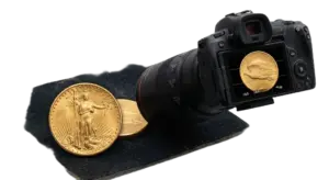 A close-up photograph of a camera and lens set up to take a detailed macro picture of a gold Saint-Gaudens Double Eagle coin on a dark felt mat, illustrating the process of photographing rare coins for authentication.