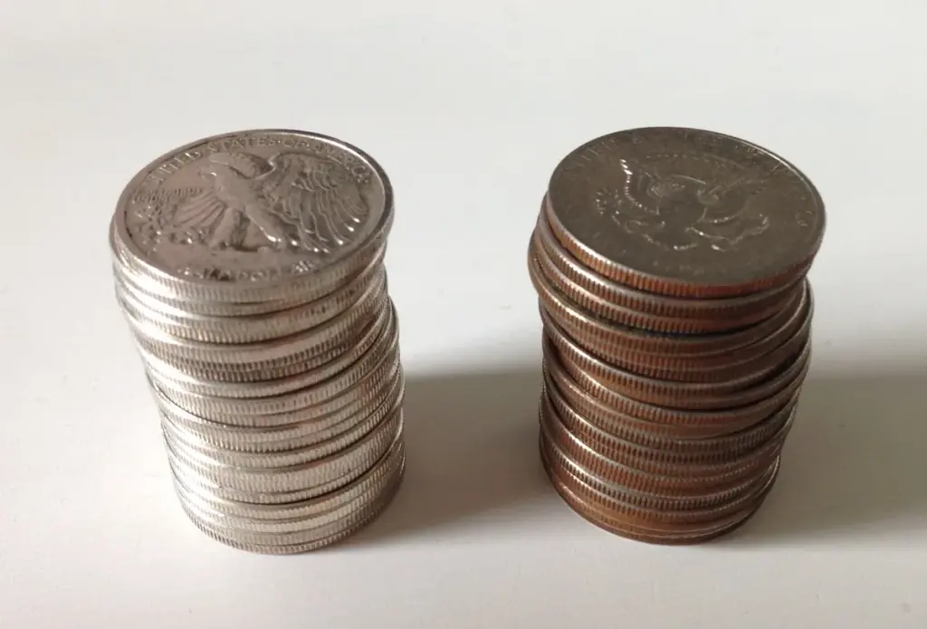 Two stacks of U.S. half dollars: 90 percent silver Walking Liberty halves with bright silver edges beside copper-nickel clad Kennedy halves with copper-colored edges