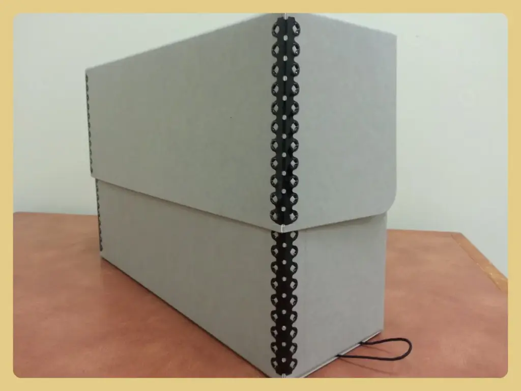 Gray acid-free archival document box with a metal-edged lid on a table