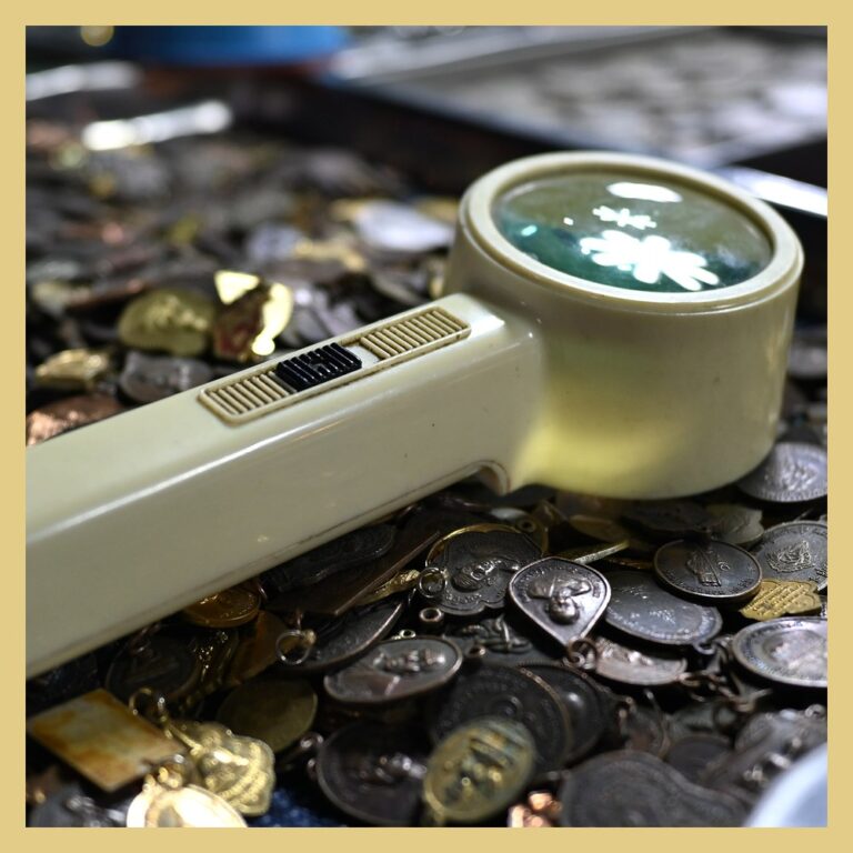 Hand magnifier resting on a pile of old coins and medals during a coin collection appraisal