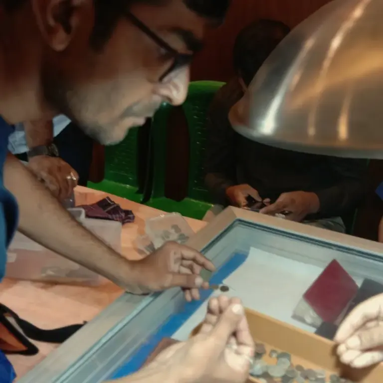 Man in glasses closely examining a coin between his fingers over a display case of coins