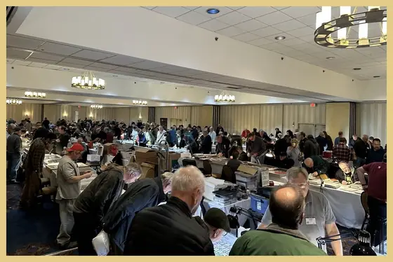 Men examining coins at dealer tables in a busy coin show hall