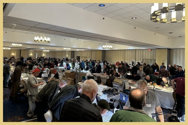 Men examining coins at dealer tables in a busy coin show hall
