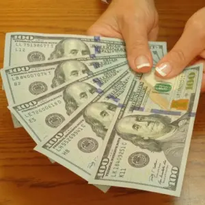 Photo of hands fanning out five $100 bills, representing fast payment for coins