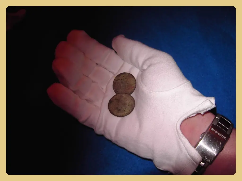 A curator's hand in a white cotton glove holding two old coins