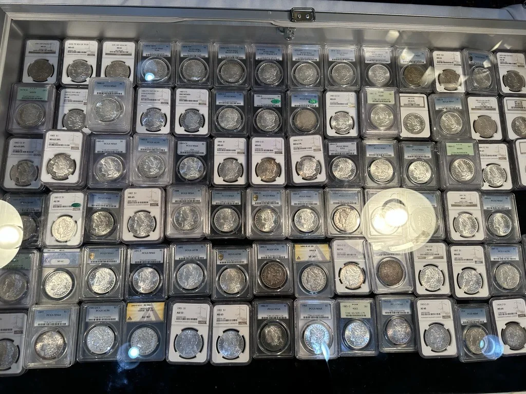 Dealer display case filled with rows of graded silver dollars in plastic holders at a coin show