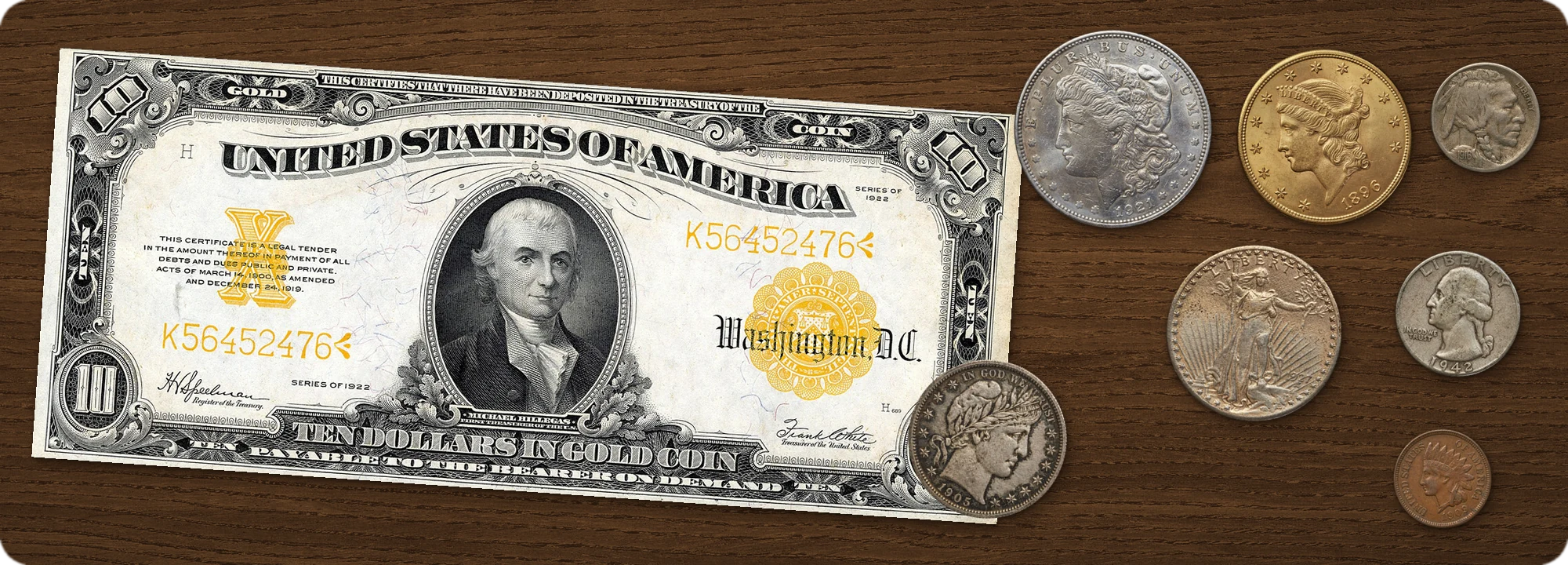 A coin collection laid out on a walnut tabletop at true relative size: a 1922 $10 gold certificate, a 1921 Morgan silver dollar, an 1896 Liberty Head $20 gold double eagle, a 1927 Saint-Gaudens $20 gold double eagle, a 1905 Barber half dollar, a 1916 Buffalo nickel, a 1942 Washington quarter and a 1909 Indian Head cent