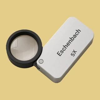 Lupa plegable moderna con Eschenbach y 5X impresos en su cuerpo plateado y aro negro, usada para una tasación gratuita de monedas