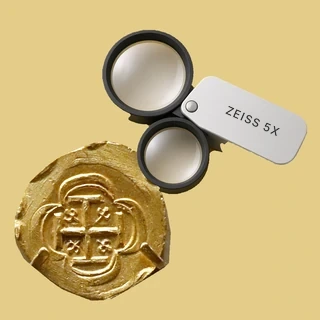 Lupa doble plegable con Zeiss 5X impreso, junto a una moneda de oro de 2 escudos de México de 1714, usada para una tasación gratuita de monedas