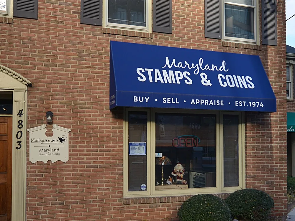 Brick storefront of a local coin and stamp shop with a blue awning reading Buy, Sell, Appraise