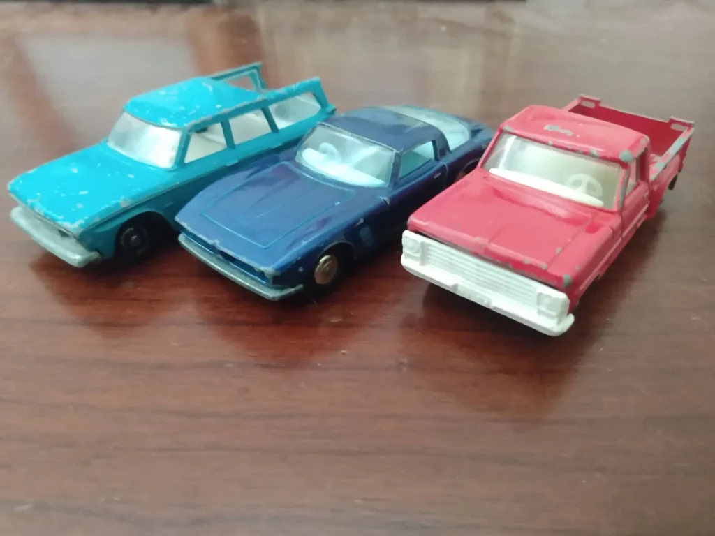 Three vintage 1960s Lesney Matchbox die-cast model cars in turquoise, blue and red on a wooden table